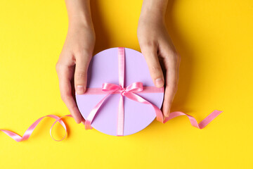 Female hands and round gift box with bow on yellow background