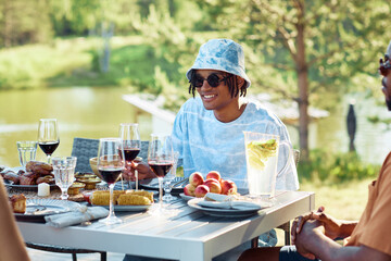 Portrait of young black man smiling at table while enjoying dinner party with friends outdoors in Summer