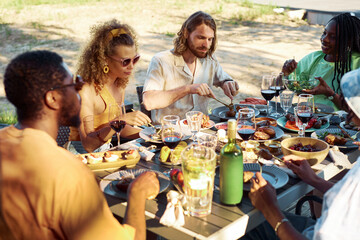 Diverse group of people enjoying dinner together outdoors in Summer sitting at table with delicious homemade feast