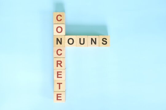 Concrete nouns concept in English grammar noun education. Wooden block crossword puzzle flat lay in blue background.