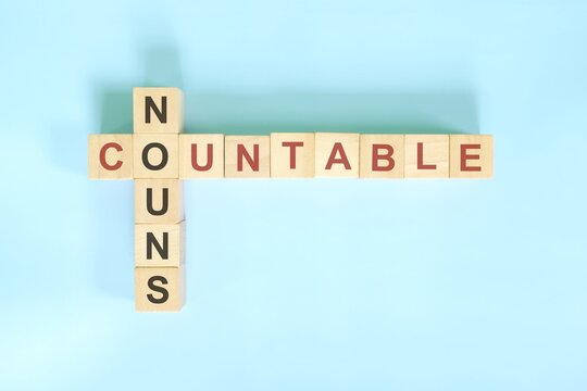 Countable nouns concept in English grammar noun education. Wooden block crossword puzzle flat lay in blue background.