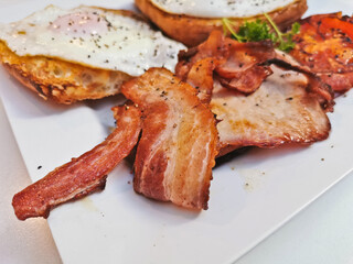 Big English breakfast with sunny fried eggs, bacon, tomatos, ham on Turkish flat grilled bread on white dish