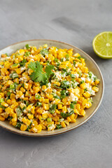Homemade Mexican Street Corn Esquites on a Plate on a gray surface, side view.