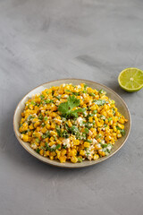 Homemade Mexican Street Corn Esquites on a Plate on a gray background, side view.