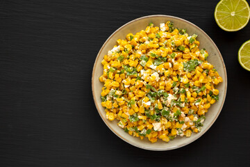 Homemade Mexican Street Corn Esquites on a Plate on a black background, top view. Flat lay, overhead, from above. Copy space.