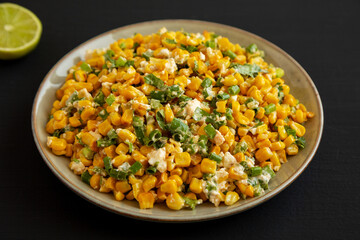 Homemade Mexican Street Corn Esquites on a Plate on a black background, side view.