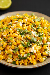 Homemade Mexican Street Corn Esquites on a Plate on a black surface, side view. Close-up.