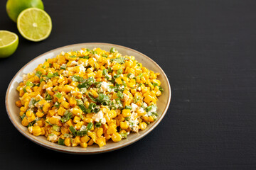 Homemade Mexican Street Corn Esquites on a Plate on a black background, side view. Copy space.