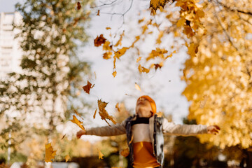 Kid having fun in autumn park with fallen leaves, throwing up leaf. Child boy outdoors playing with...