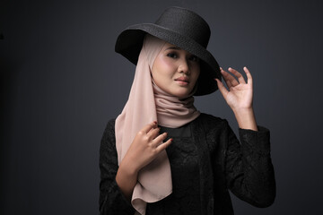 Naklejka na ściany i meble Portrait of a female  wearing a hijab, a form of lifestyle garments for Muslim women, isolated on a dark background. Eid festive and hijab fashion concept
