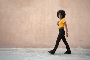 Fototapeta premium Smiling fashionable afro american woman walking on city street