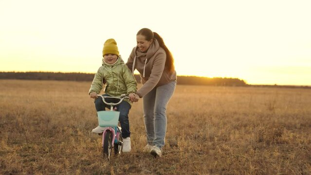 mother teaches little daughter ride two-wheeled bike at sunset, child pedals on bicycle in sunshine, outdoor outdoor activities, exercise at dawn travel, happy family life, childhood dream drive