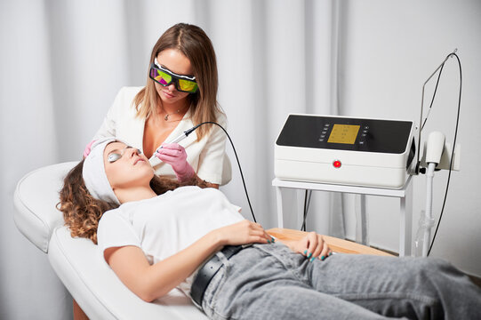 Modern treatment of telangiectasias on skin. Beautician performing local high-precision removal of dilated small vessels on woman face with innovative yellow laser.