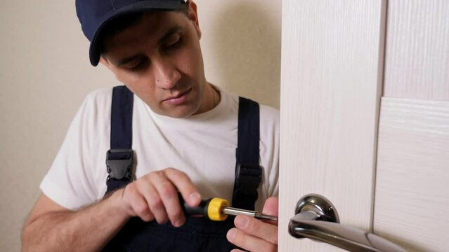Portrait of young locksmith workman in blue uniform installing door knob.