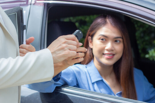 Beautiful young woman car salesman holding car keys and handing it to Asian female customer.