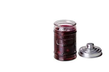 Open glass jar with cherry jam on a white background. There is a jar lid next to it.