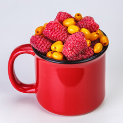 Red mug full of ripe berries (raspberry and sea buckthorn) on a white background
