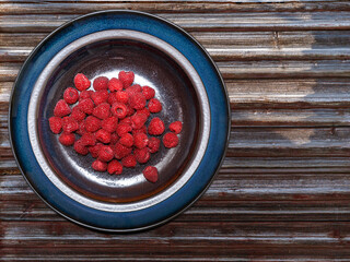 A rustic plate with fresh raspberries on the table made of wooden planks
