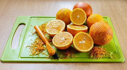 Fotobehang Sliced and peeled oranges and orange zest lie next to a paring knife on a green cutting board © Вадим Шерезданов