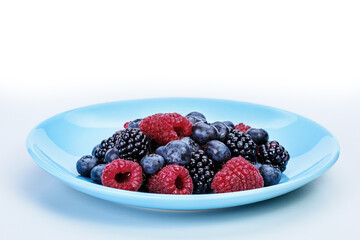 Blue plate with summer raspberries, blueberries and mulberries lying in it