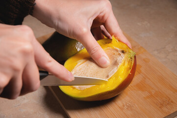 Fresh ripe organic yellow mango cut into halves. Woman cutting mango on wooden cutting board