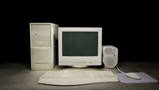 Old dirty computer with vintage monitor sitting on a dark table on a black background. With a vintage mouse, mousepad and keyboard. Next to a vintage old audio speaker. 3D rendering