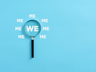 Magnifying glass magnifies the word WE surrounded with the words ME.