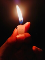 Fingers holding a small ignited candle in a dark background