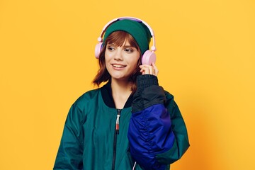 horizontal photo of a beautiful woman in a jacket and hat listening to music with pink headphones holding them with her hands