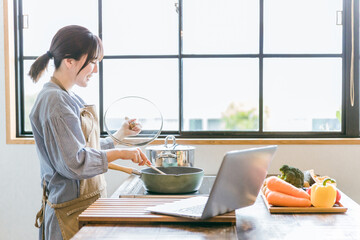 パソコンでレシピ動画を見ながら料理をする女性
