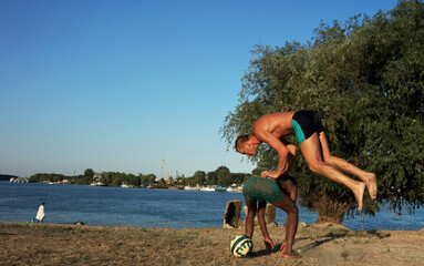 man jumping over another man on a beach in summer at sunset