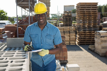 African american man manager working in an open air warehouse keeps records of construction...