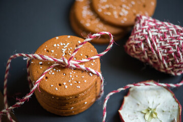 a stack of round-shaped gingerbread cookies tied with a thread of red woolen yarn on a dark background