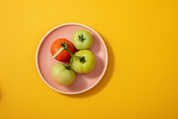 Yellow and green tomatoes on a pink plate on a light background. blank background for design