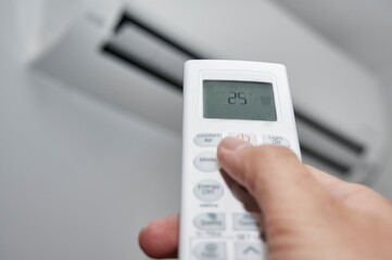 Hand of a man pressing the buttons on the control of a split air conditioner to turn it on at the...