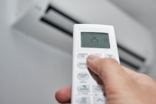 Hand of a man pressing the buttons on the control of a split air conditioner to turn it on at the recommended temperature of 25 degrees Celsius