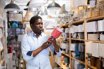 Portrait of interested focused african american man choosing light fixture for home interior design...