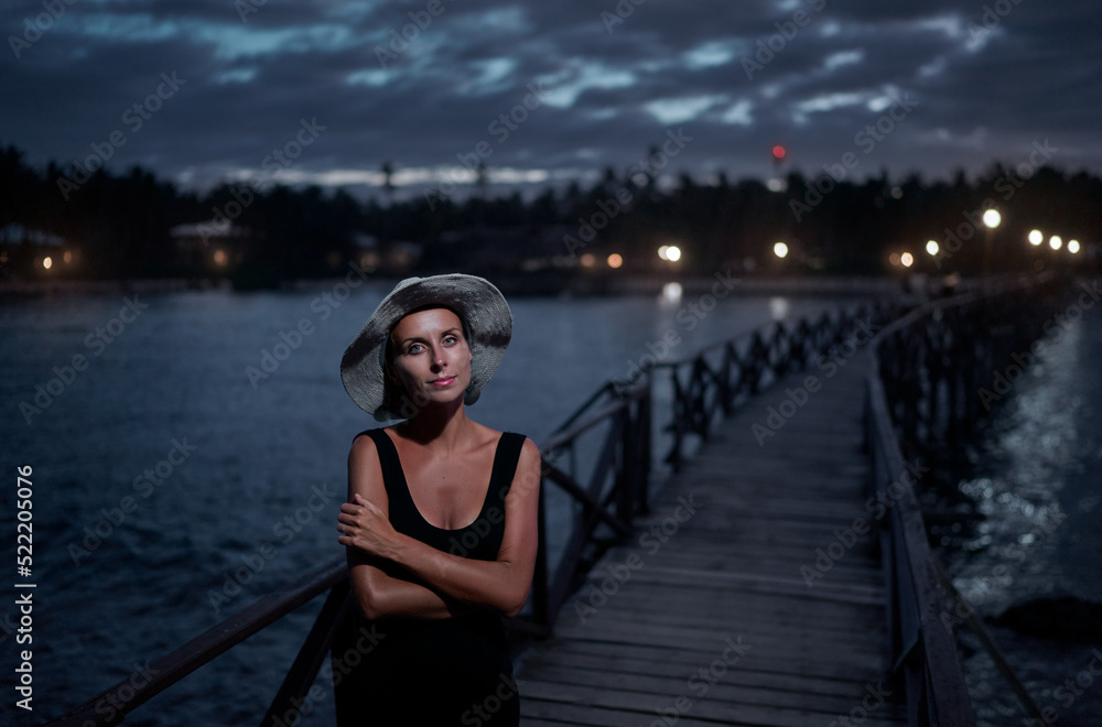 Wall mural Vacation on tropical island. Young woman in hat enjoying sea view from wooden bridge terrace at night time, Siargao Philippines.