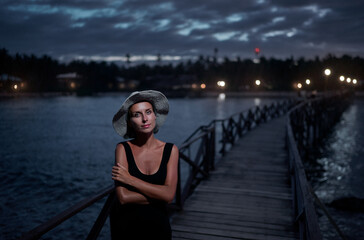 Vacation on tropical island. Young woman in hat enjoying sea view from wooden bridge terrace at night time, Siargao Philippines.