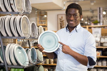Portrait of cheerful african american man demonstrating new ceramic plate bought at household goods...