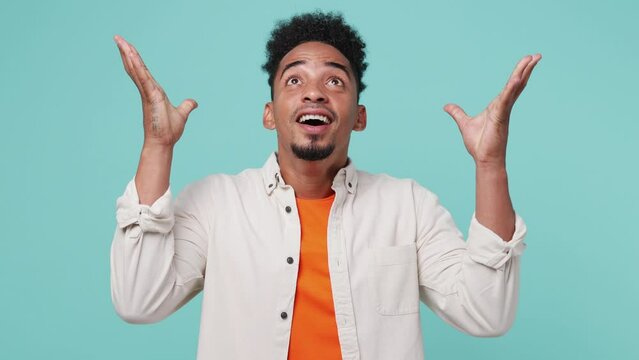 Young looking surprised man of African American ethnicity 20s he wear shirt t-shirt wow showing hands brain explosion head isolated on plain pastel light blue cyan background. People lifestyle concept