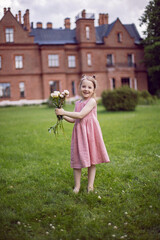 portrait of a beautiful baby girl in a pink dress standing with a bouquet of flowers pions on a green meadow in summer