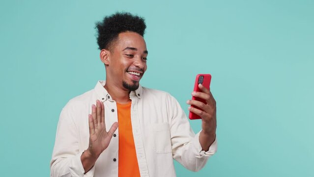 Young man of African American ethnicity wear shirt t-shirt get video call use mobile cell phone do selfie talk conduct pleasant conversation greet isolated on plain pastel light blue cyan background