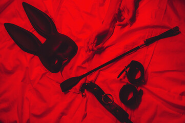 set of BDSM accessories with female hands is lying on bed. Flogger whip, handcuffs, mask and choker...