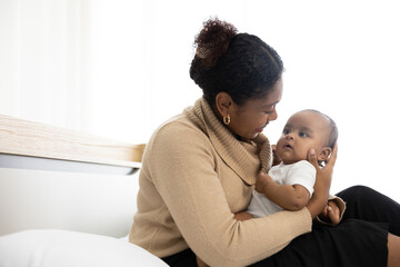 African young mother hugging and playing with her adorable baby on bed