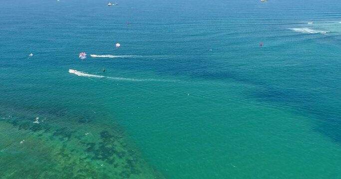 Aerial shot of parasailing boats going over turquoise water
