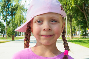 An emotional, cheerful girl with pigtails and a baseball cap to one side. Stylish preschooler. Naughty girl on the street in the park. Cheerful funny child
