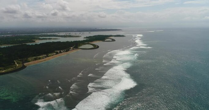Aerial shot of waves crashing over colorful reef in front of a tropical island