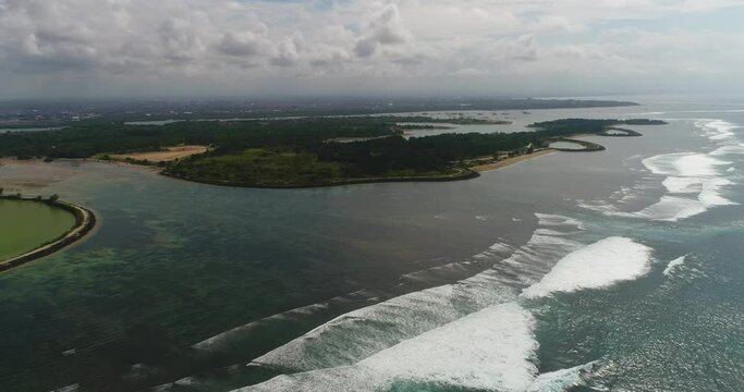Aerial shot of waves crashing over colorful reef in front of a tropical island