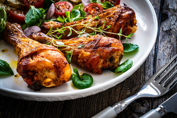 Barbecue chicken drumsticks with fried potato, lettuce and mini tomatoes on wooden table
